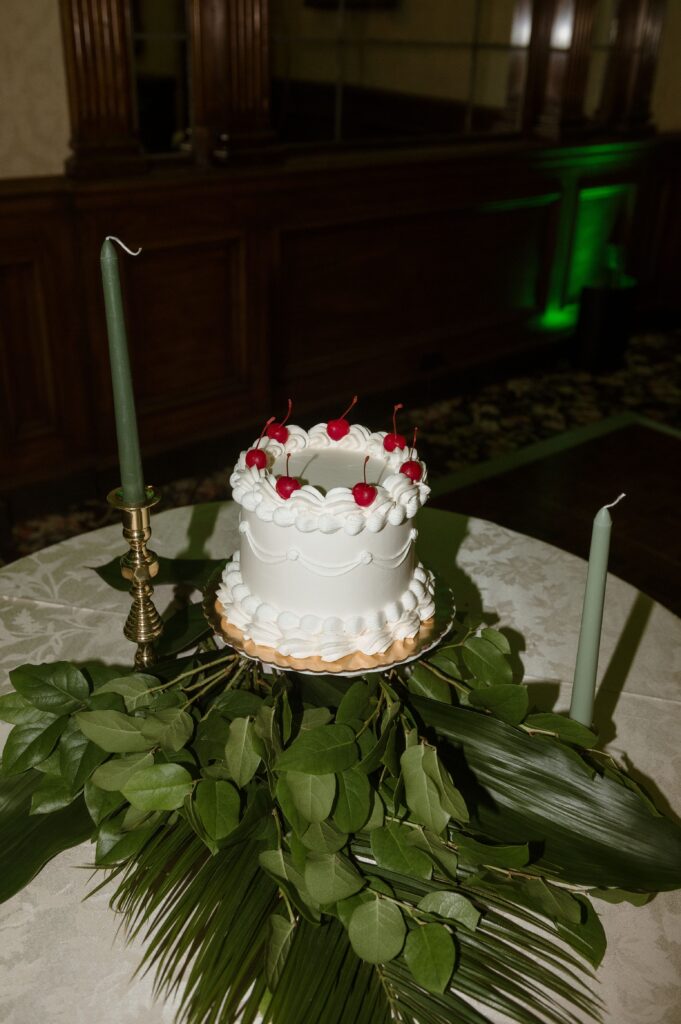 A white cake with cherries sits atop greenery at a wedding reception at the Pfister Hotel