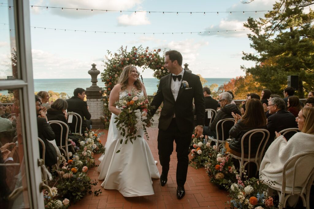 Newly wed couple walks down the aisle smiling at Villa Terrace