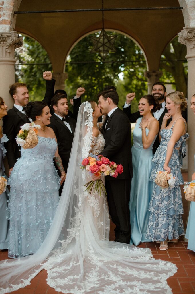 Bride and groom kiss while their bridal party cheers