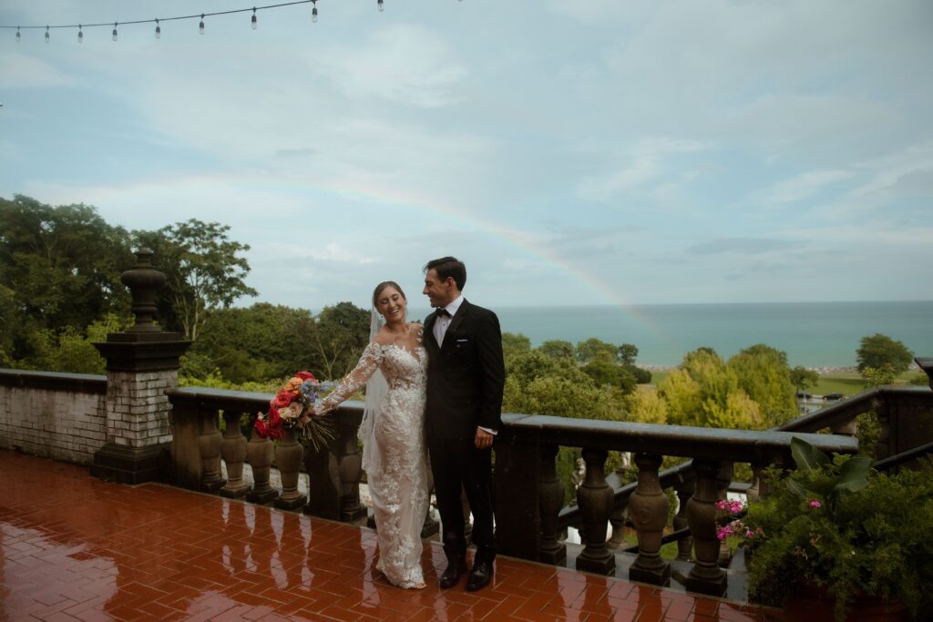 Bride and groom smile in front of a rainbow